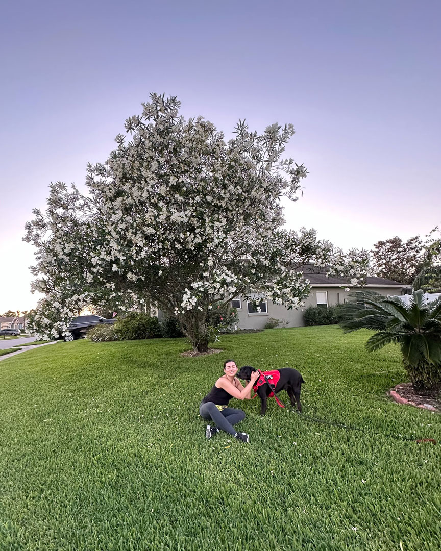 Rada and her dog cuddling under a big tree covered in white flowers.